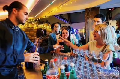 Traiteur Kidira Traiteur  Maromme #1 Un barman sert un verre de vin rouge à une femme lors d'un événement dans un bar éclairé par des guirlandes lumineuses.