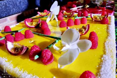 Traiteur Kidira Traiteur  Maromme #2 Gâteau décoré de framboises, fleurs en sucre et fruits de la passion sur un glaçage jaune vif.