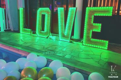 Traiteur Kidira Traiteur  Maromme #4 Lettres lumineuses formant le mot ’LOVE’ éclairées en vert, entourées de ballons blancs et dorés près d'une piscine.