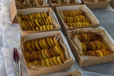 Traiteur Gusto e cucina Menucourt #5 Buffet en plein air avec des boîtes contenant des biscuits, des pâtes et des beignets disposés sur une nappe blanche.