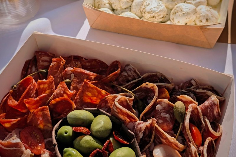 Antipasti Tagliere di salumi / ©Gusto e cucina Plateau de charcuterie avec olives, tomates et viandes variées, accompagné de mozzarella et antipasti en arrière-plan.