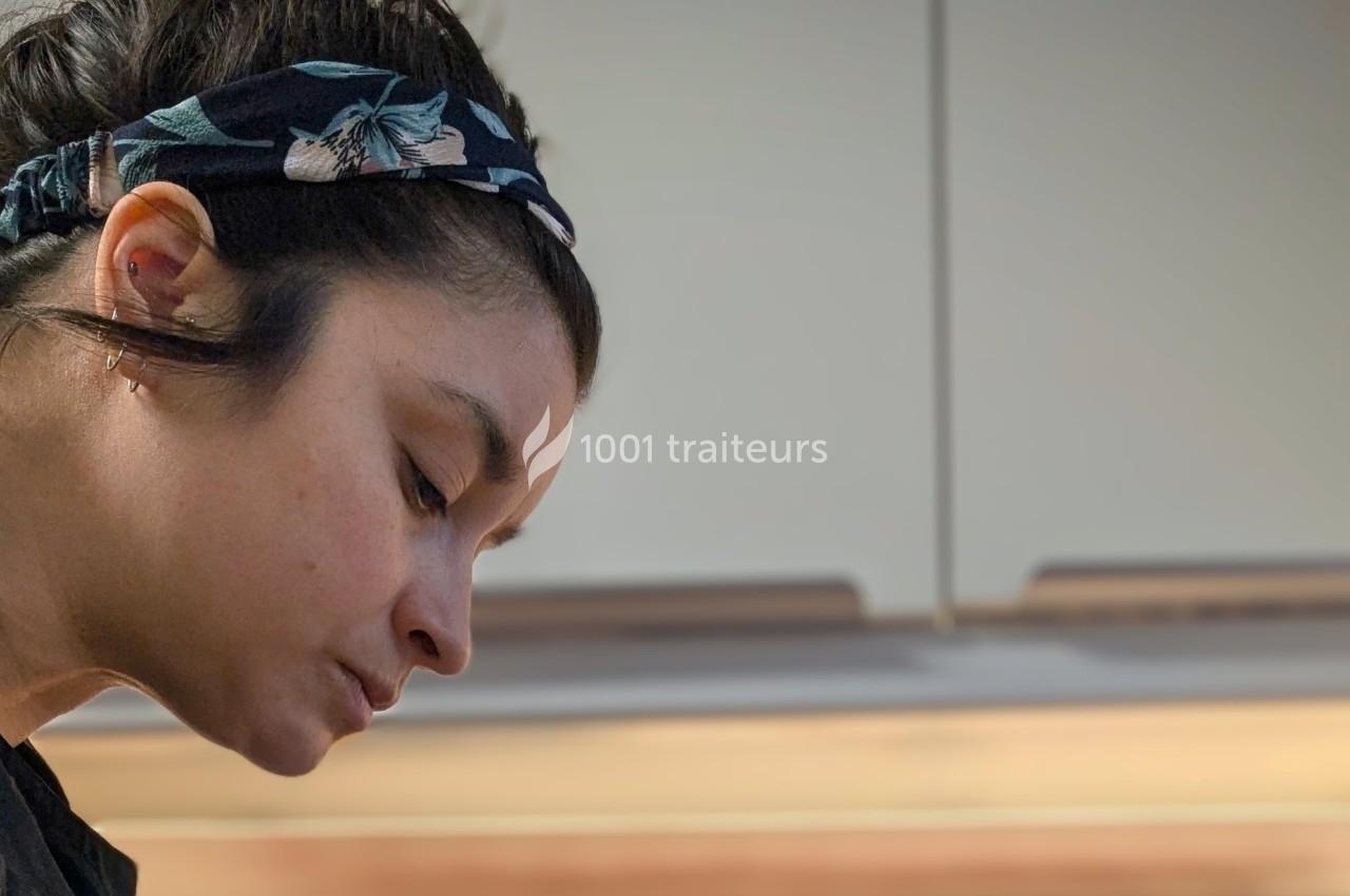 Femme concentrée, portant un bandeau fleuri, vue de profil dans un intérieur avec des meubles de cuisine en arrière-plan.