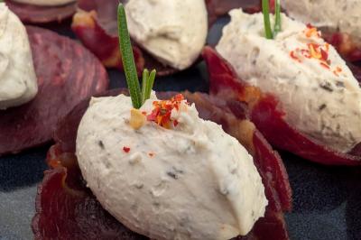 Tranches de viande séchée garnies de quenelles de fromage frais aux herbes, décorées de brins de romarin et de piment.