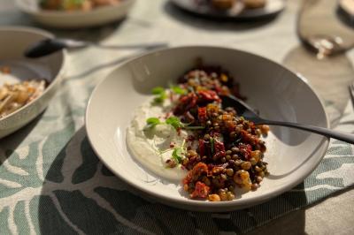 Assiette de lentilles garnies de légumes rôtis et herbes fraîches, accompagnée de sauce blanche, sur une table éclairée par…
