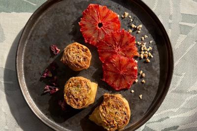 Assiette contenant des rouleaux de pâte dorés, des tranches d'orange sanguine et des éclats de noisettes.
