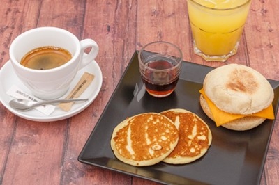 Petit-déjeuner composé d'un café, d'un jus d'orange, de pancakes, d'un muffin garni de fromage et d'un sirop.