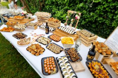 Table garnie de divers amuse-bouches et plats apéritifs disposés sur des plateaux dans un jardin verdoyant.