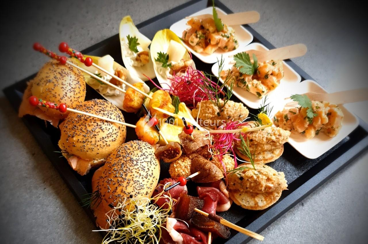 Plateau de bouchées apéritives variées comprenant mini-burgers, tartinades, brochettes et légumes frais.
