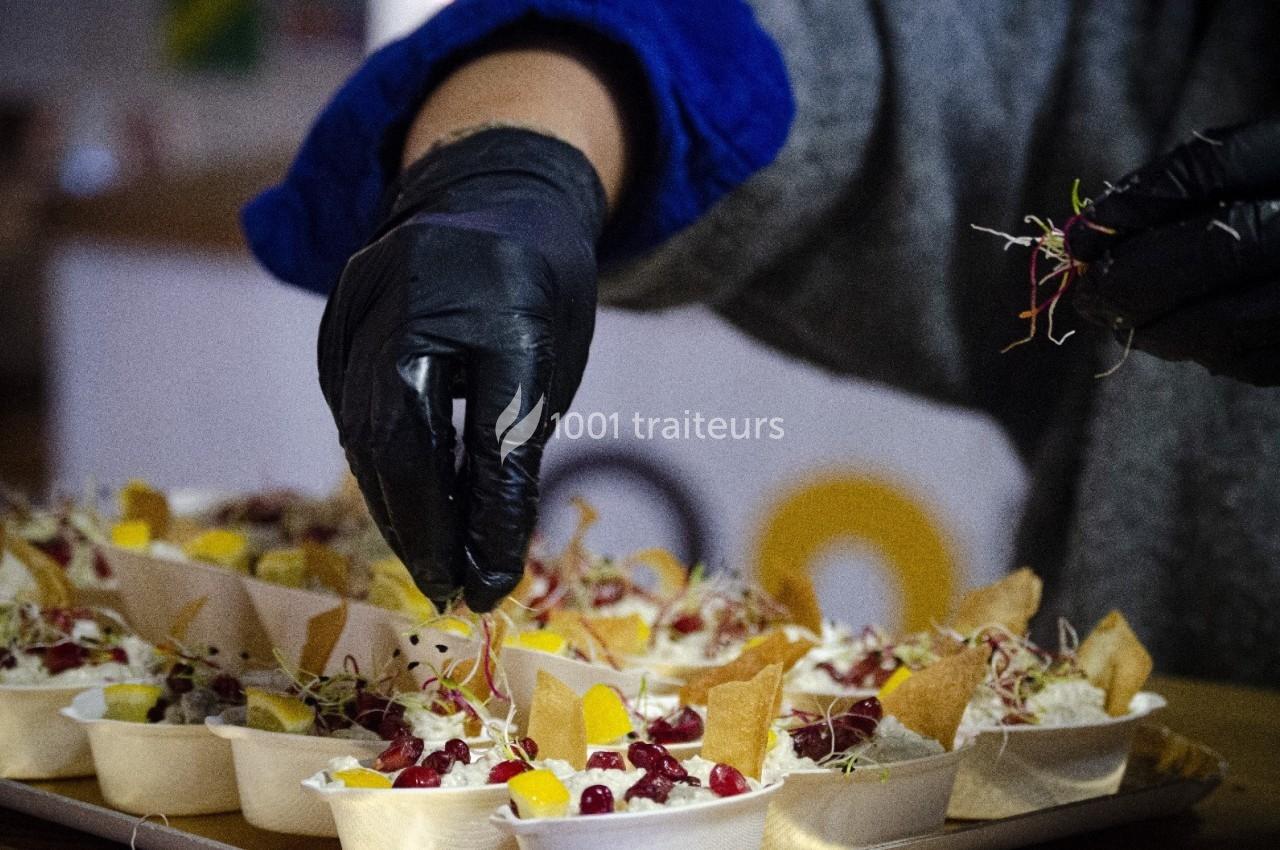 Une personne garnit des plats individuels avec des pousses et des morceaux de fruits colorés.