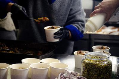 Une personne sert de la nourriture dans des gobelets, avec des graines visibles dans un bocal au premier plan.