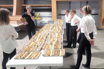 Traiteur Aux Saveurs du Jour Chemillé #4 Des serveuses en tenue professionnelle observent une longue table garnie de plateaux de bouchées apéritives.