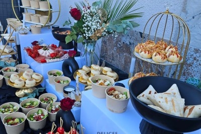 Buffet extérieur avec mini-sandwichs, salades, wraps et desserts, décoré de fleurs et éléments dorés.