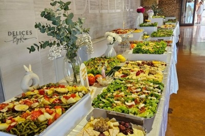 Buffet varié avec salades, fromages, fruits et décorations florales, présenté sur une longue table blanche.