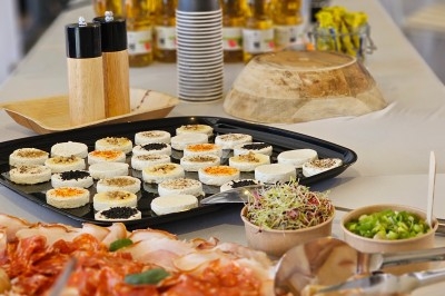 Plateau de charcuterie, fromages et condiments disposés sur une table de buffet avec huiles et épices en arrière-plan.