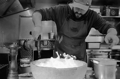 Un cuisinier fait flamber un plat dans une grande meule de fromage dans une cuisine professionnelle.