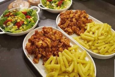 Assiettes de pâtes jaunes accompagnées de poulet en sauce et salades colorées servies dans des bols.