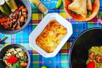 Traiteur Doucines Créoles Courbevoie #3 Repas coloré composé de plats créoles variés, avec légumes, gratin, samoussas, canne à sucre et piments sur une nappe à…