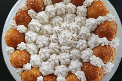 Traiteur Doucines Créoles Courbevoie #4 Gâteau composé de choux caramélisés et de crème disposés en cercle sur un fond noir.