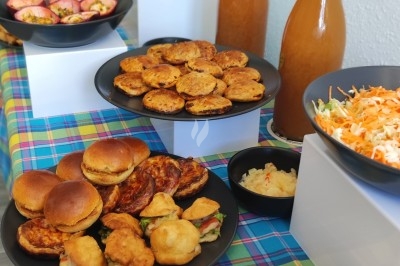 Traiteur Doucines Créoles Courbevoie #2 Buffet avec assiettes de mini-burgers, beignets, crudités, jus en bouteilles et salades sur une nappe colorée.