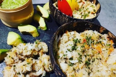 Traiteur Doucines Créoles Courbevoie #5 Assiettes de crabe émietté assaisonné, servies dans des coques de noix de coco avec des tranches d'avocat et une sauce verte.