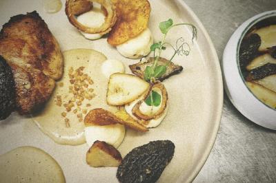 Assiette gastronomique avec viande grillée, purée, morilles, chips et sauce, accompagnée d'un bol de légumes.