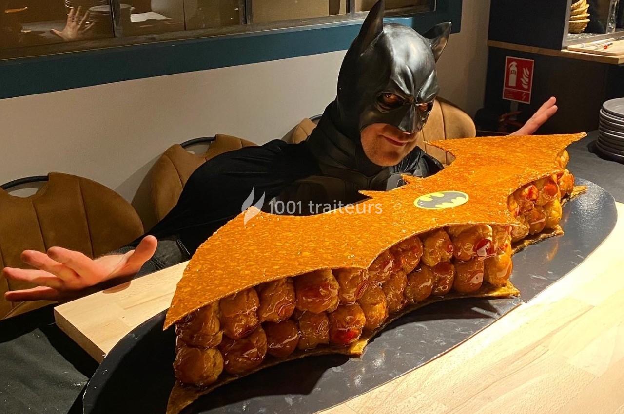 Traiteur La Fringale  Buc #1 Un homme déguisé en Batman pose derrière une pièce montée en forme de logo de chauve-souris.
