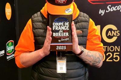 Traiteur Burger Park Rioz #1 Un homme tenant un trophée marqué ’Coupe de France du Burger 2025’ devant son visage, portant une casquette et une veste.