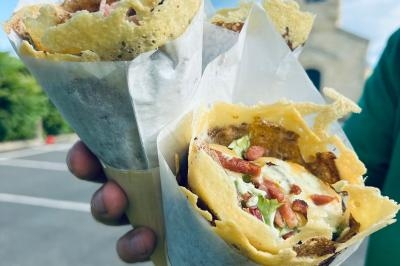 Deux cônes de galettes croustillantes garnies de salade, fromage et lardons, tenus à la main en extérieur.