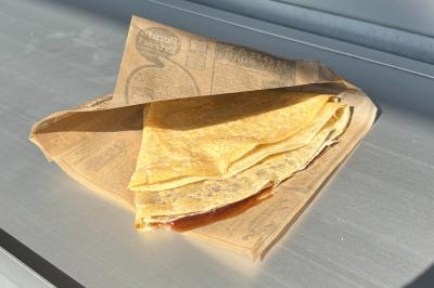 Traiteur Korrigans Foodtruck Meaux #5 Crêpe pliée dans un papier brun imprimé, posée sur une surface métallique éclairée par la lumière naturelle.