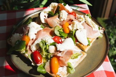 Traiteur Pasta Da Nonna Mia Bouc-Bel-Air #5 Assiette de tartines garnies de jambon cru, mozzarella, tomates cerises et mâche sur une nappe à carreaux rouges.