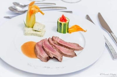 Traiteur Traiteur Benoit Bruley Épagny #3 Assiette gastronomique avec tranches de viande, sauce, courgette farcie et fleur comestible en décoration.