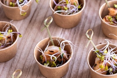 Petits pots en carton contenant des bouchées garnies de crevettes, pousses germées et brochettes en bois.