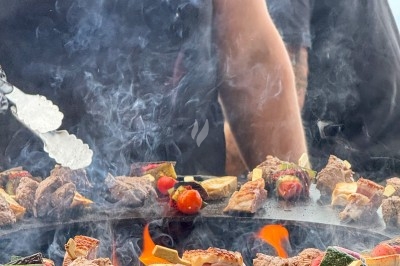 Traiteur Traiteur D'azur Saint-Vallier-de-Thiey #4 Viande et légumes grillés sur une plancha avec des flammes, cuisinés par une personne en polo noir.