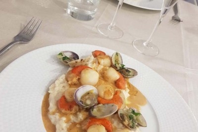 Assiette de risotto crémeux garni de noix de Saint-Jacques, coques et sauce, servie sur une table dressée.