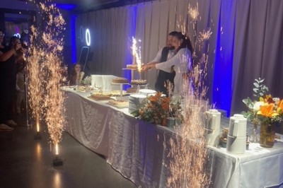 Un couple coupe un gâteau de mariage entouré de fontaines lumineuses, dans une salle décorée avec des fleurs et des lumières…