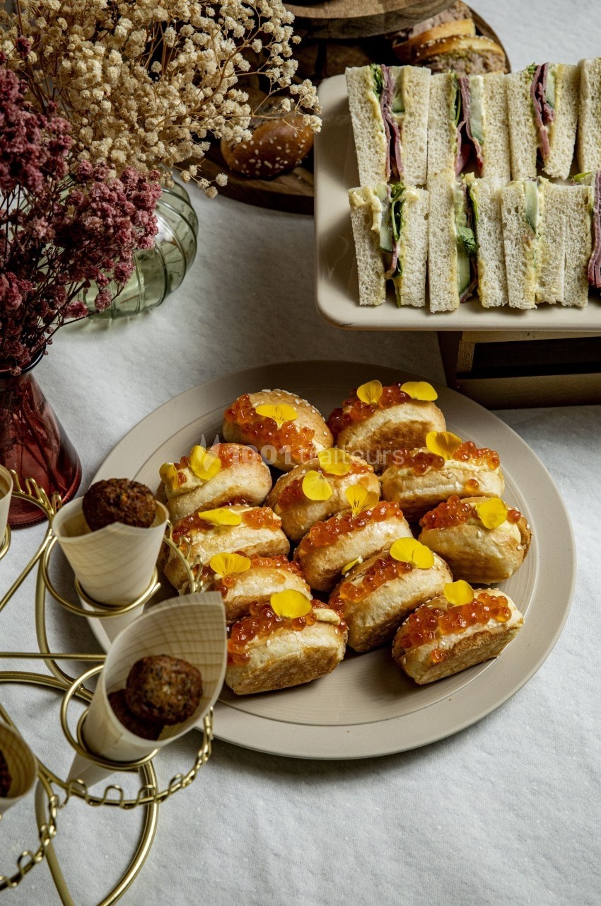 Assortiment de sandwichs, petits pains garnis de saumon et canapés, disposés sur une table décorée de fleurs séchées.