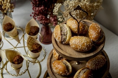 Plateau en bois avec mini-burgers au sésame, entouré de cônes en bois garnis de bouchées apéritives.