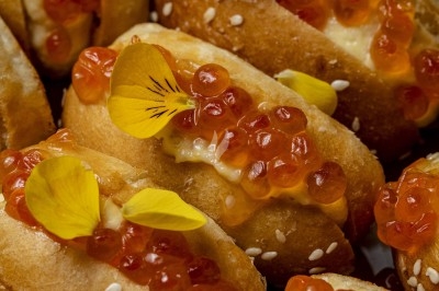 Petits pains garnis de crème, œufs de saumon et pétales jaunes, disposés en gros plan.