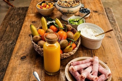 Petit-déjeuner disposé sur une table en bois avec fruits, yaourt, céréales, jus d'orange et roulés de jambon.