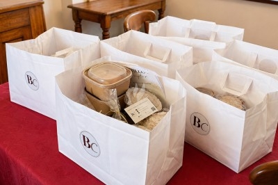 Sacs en papier blanc contenant des plats à emporter et des emballages alimentaires posés sur une table rouge.