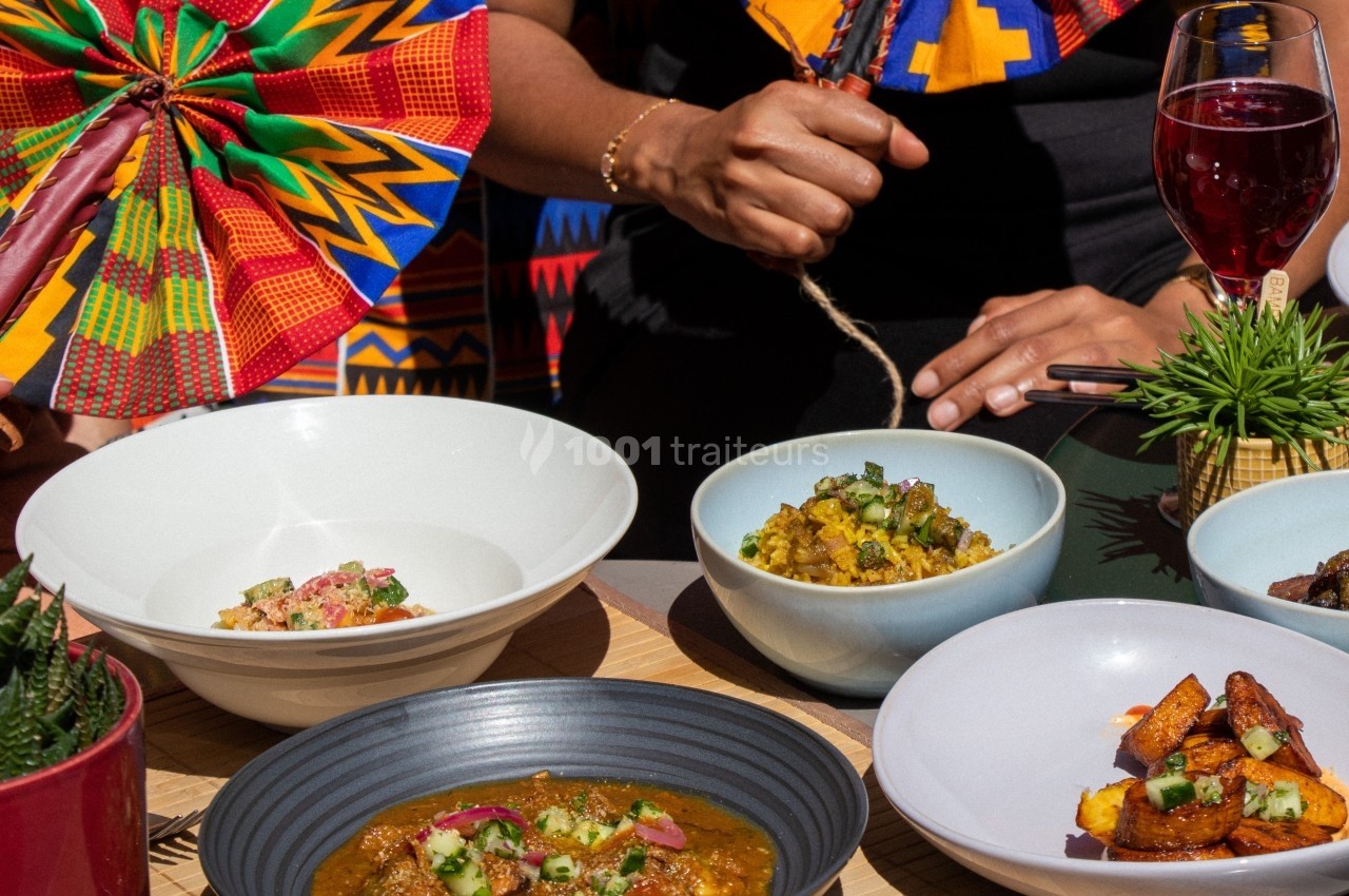 Repas coloré avec plats variés dans des bols, accompagné de boissons, sur une table décorée de motifs africains.