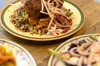 Traiteur Montagu Troyes #2 Assiette de viande servie sur un lit de quinoa avec légumes et oignons rouges, posée sur une table en bois.