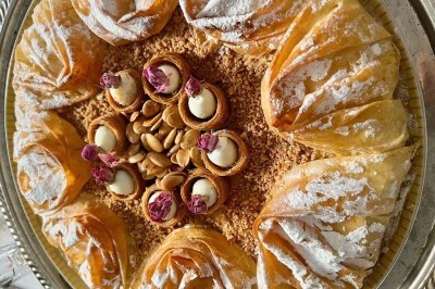 Plateau de pâtisseries orientales en pâte filo garnies d'amandes, de crème et décorées de fleurs séchées.