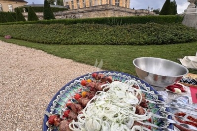 Assiette de brochettes garnies d'oignons et de légumes, présentée devant un château entouré de jardins.