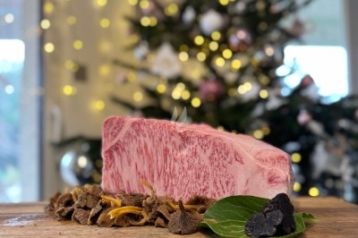 Tranche de bœuf wagyu marbrée posée sur une planche en bois avec des champignons et une truffe, sapin décoré en arrière-plan.