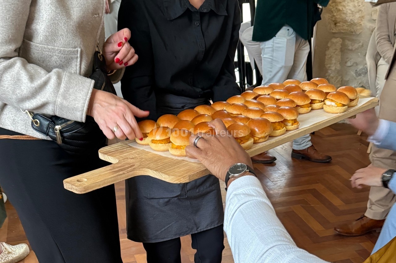Plateau en bois garni de mini-burgers servi à des convives lors d'un événement.