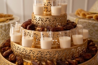 Traiteur Naylan Traiteur Claye-Souilly #5 Plateau doré à étages décoré de dattes et de verrines de lait, disposé sur une table blanche.