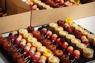 Plateau de mignardises variées comprenant cannelés, tartelettes et brochettes de fruits colorés.