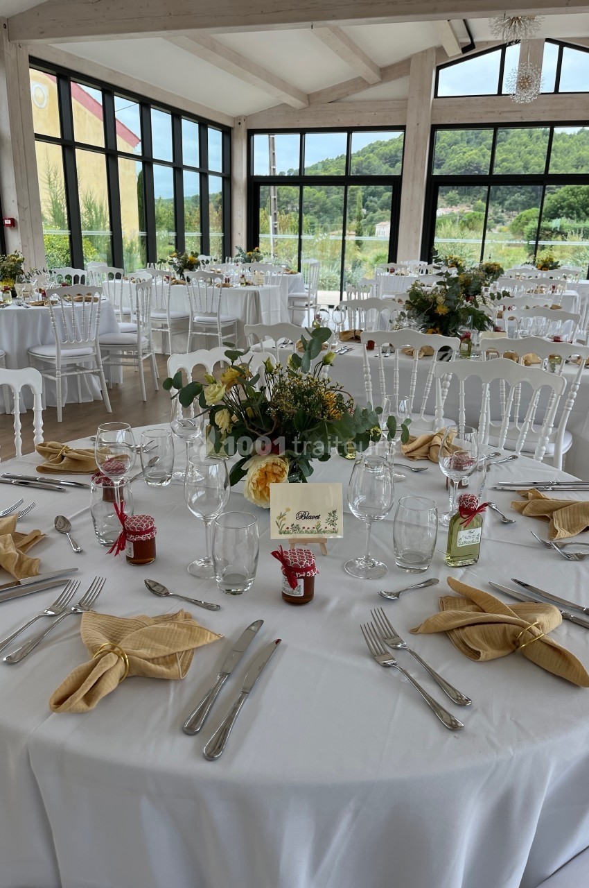 Traiteur La Cuisine By Alexandre Fréjus #1 Salle de réception lumineuse avec tables rondes dressées, nappes blanches, décorations florales et couverts élégants.
