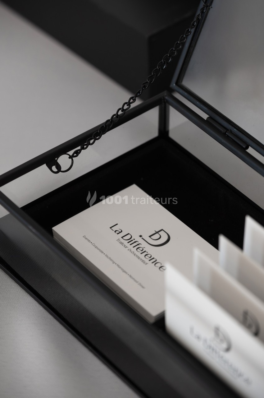 Carte de visite blanche avec logo ’La Différence’ posée dans une boîte noire ouverte avec une chaîne décorative.
